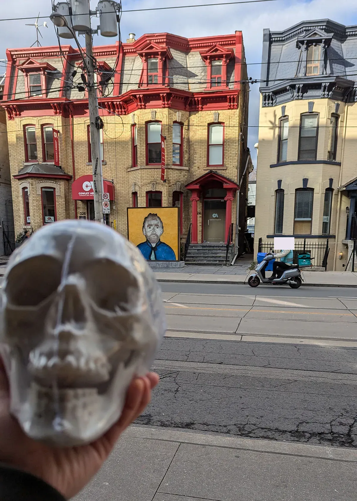 A plastic skull is being held out in front of an art installation of the artist Van Gogh&#x27;s face