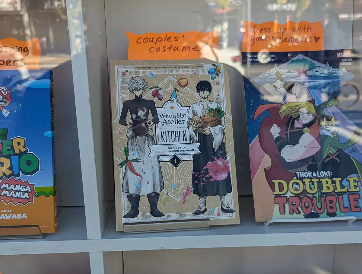 A copy of Witch Hat Kitchen volume 1 in a store window with the label "couples costume"