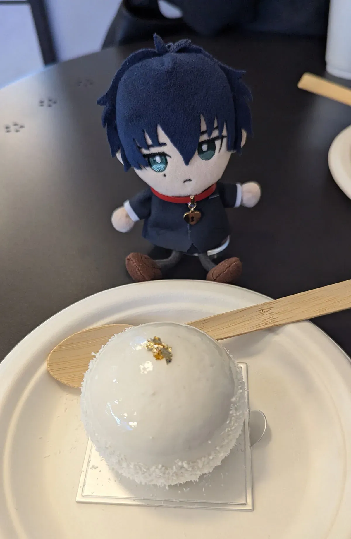 Tadashi puppet charm sits next to a passion fruit cake. The cake is white and smooth.